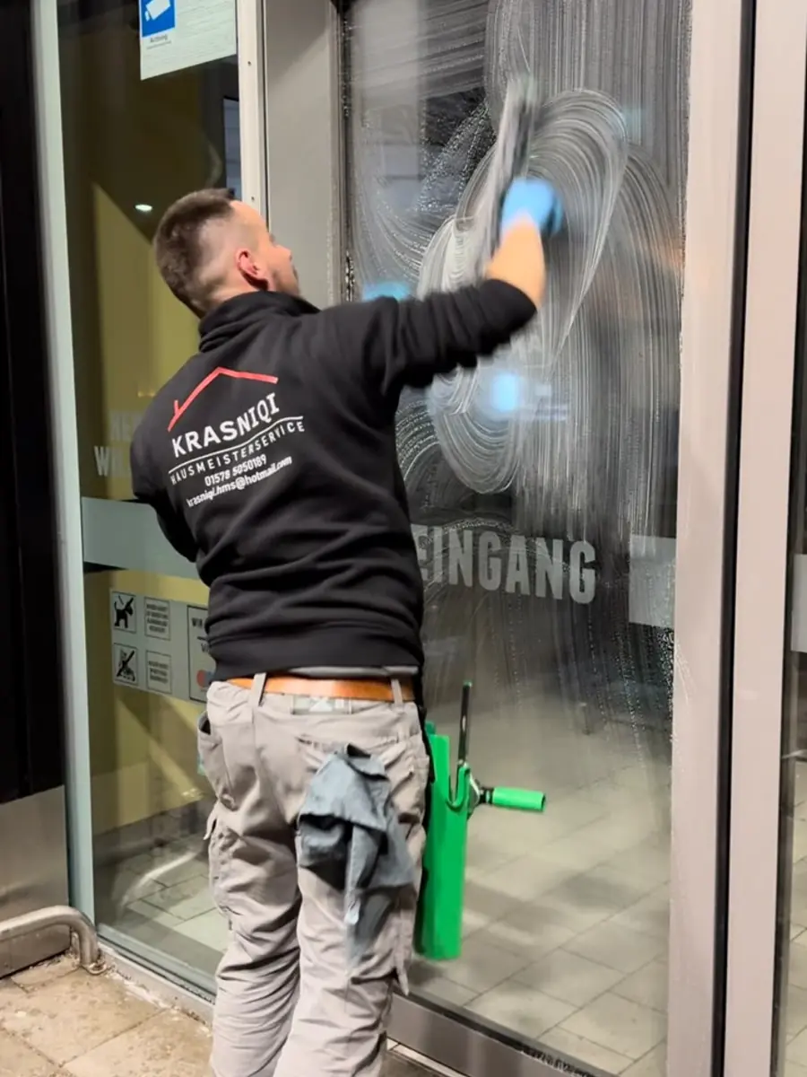 Mitarbeiter reinigt die Glasfront eines Eingangsbereichs mit dem Abzieher