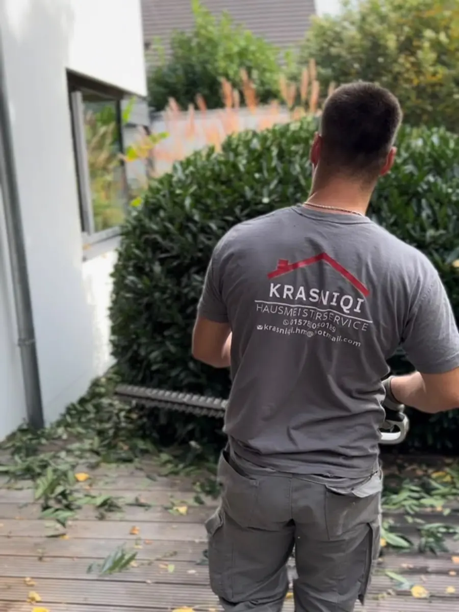 Mitarbeiter schneidet eine Hecke an einer Terrasse zurück