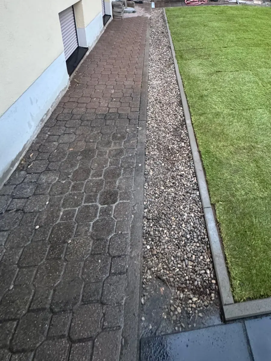 Fertiger Pflasterweg mit Entwässerungsrinne und frisch verlegtem Rollrasen